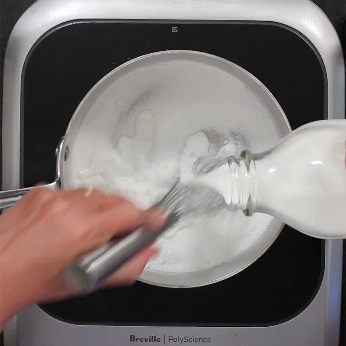 A person pouring cream into a saucepan filled with a mixture of sugar and cornstarch.