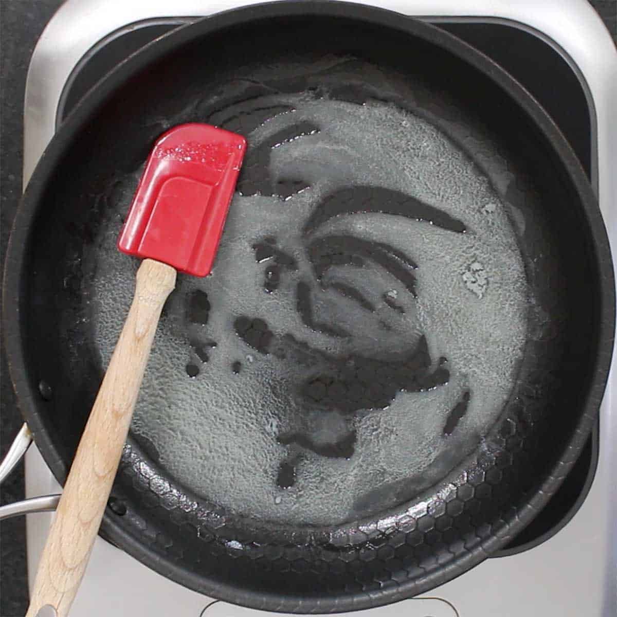 Butter that has been melted over low heat in a large black non-stick skillet with a red spatula resting in the pan.