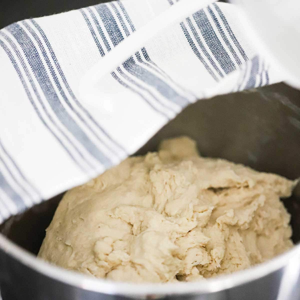 A person placing a white and blue kitchen towel over the top of a mixing bowl filled with focaccia dough.