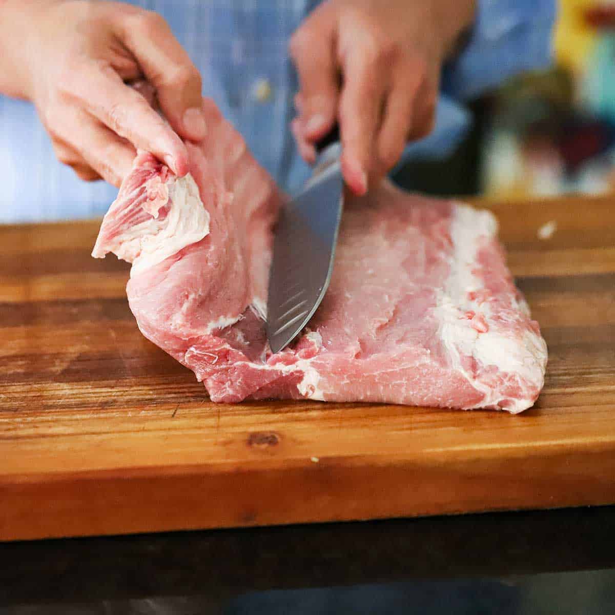 A person using a chef's knife to butterfly a pork loin roast.