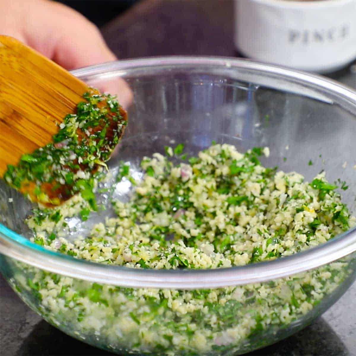 A glass bowl filled with a mixture of breadcrumbs and chopped fresh herbs.