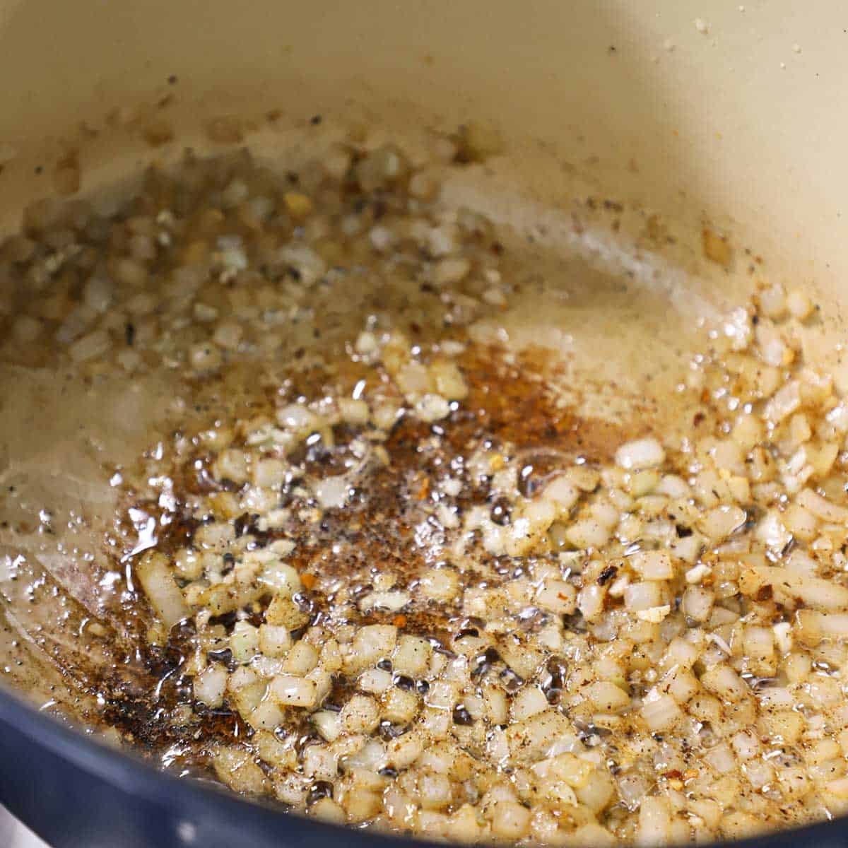 Chopped onion being sautéed in oil in a large oval Dutch oven.