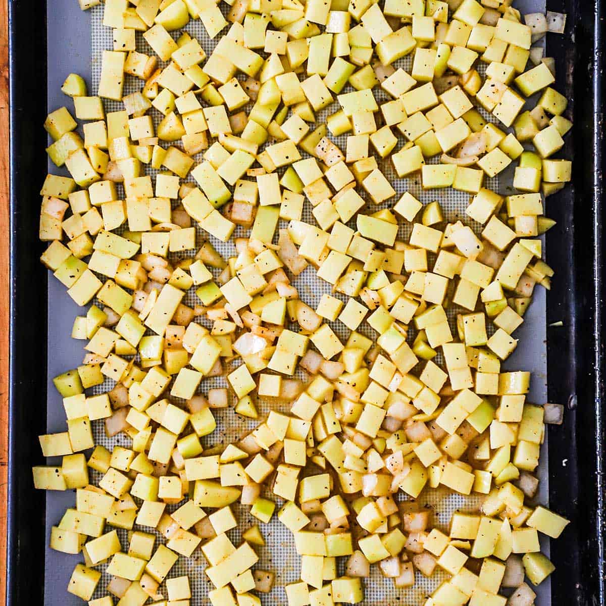 A baking sheet pan that is lined with a silicone mat topped with cubed seasoned potatoes.