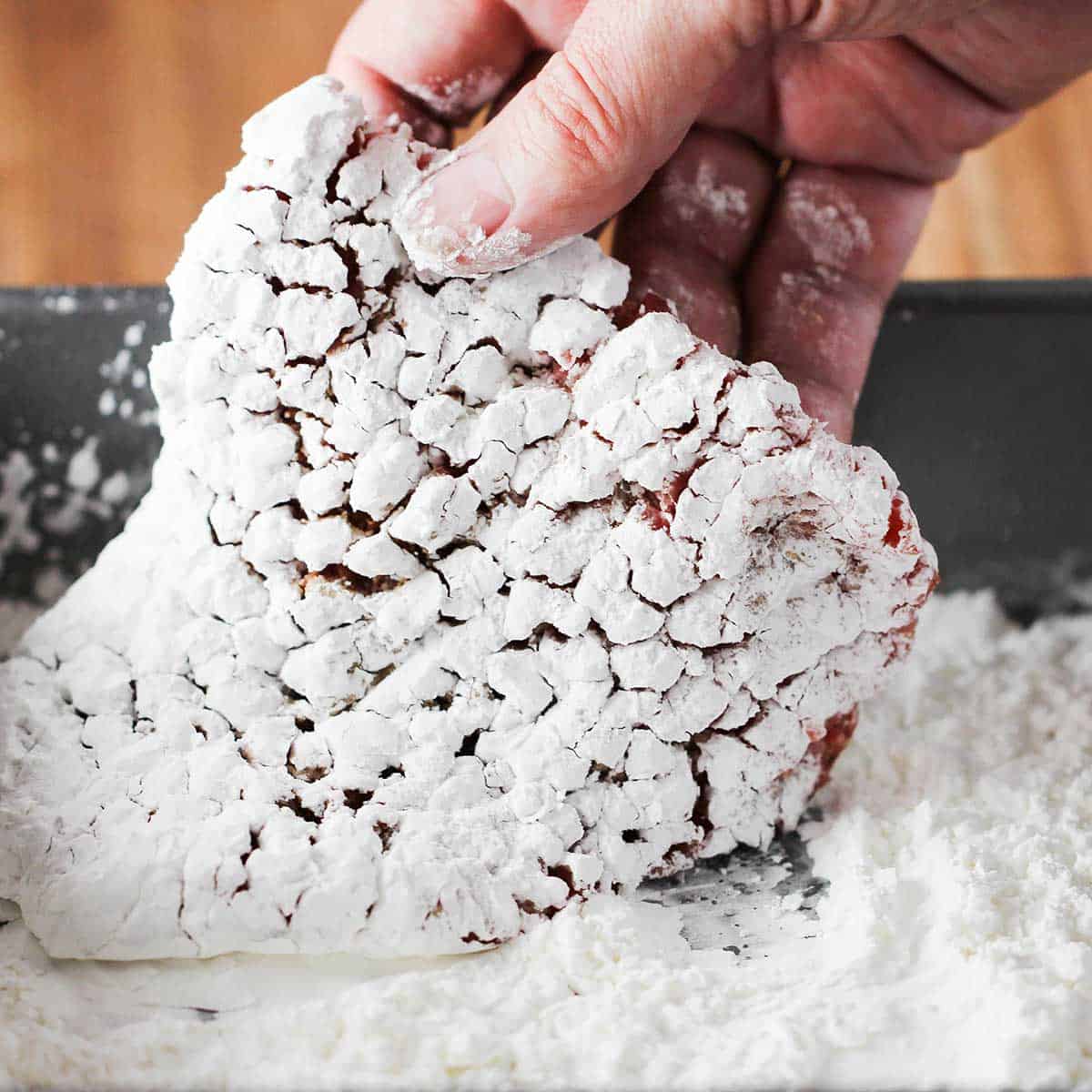 A person dredging a tenderized cubed steak in a pan filled with cornstarch.