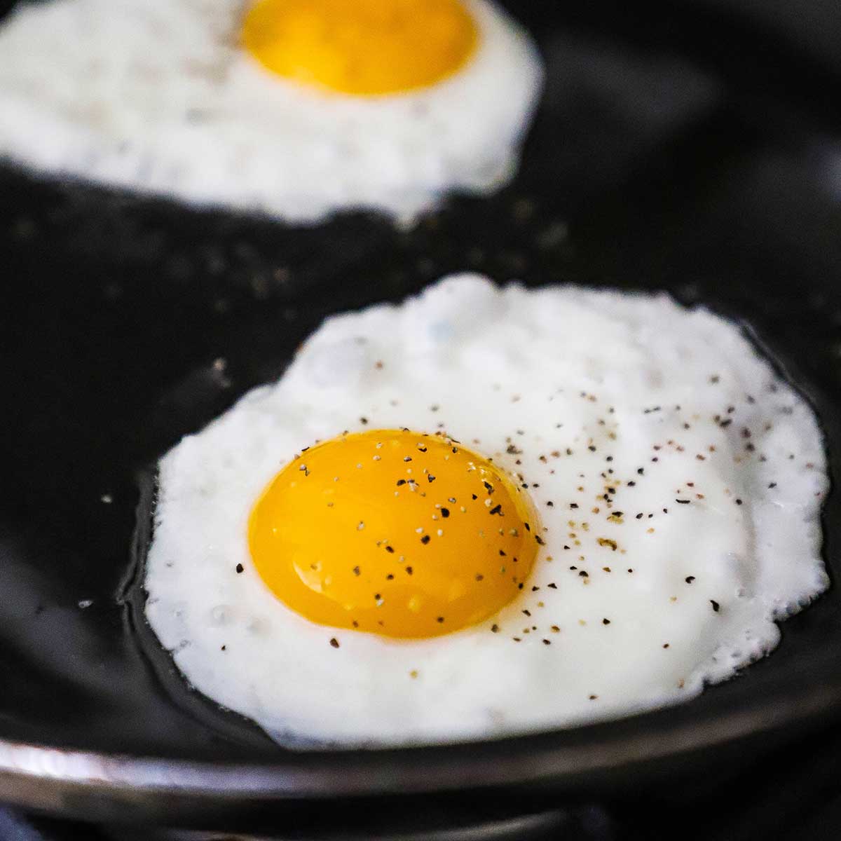 Two eggs that are being fried, sunny side up, in a large black skillet.