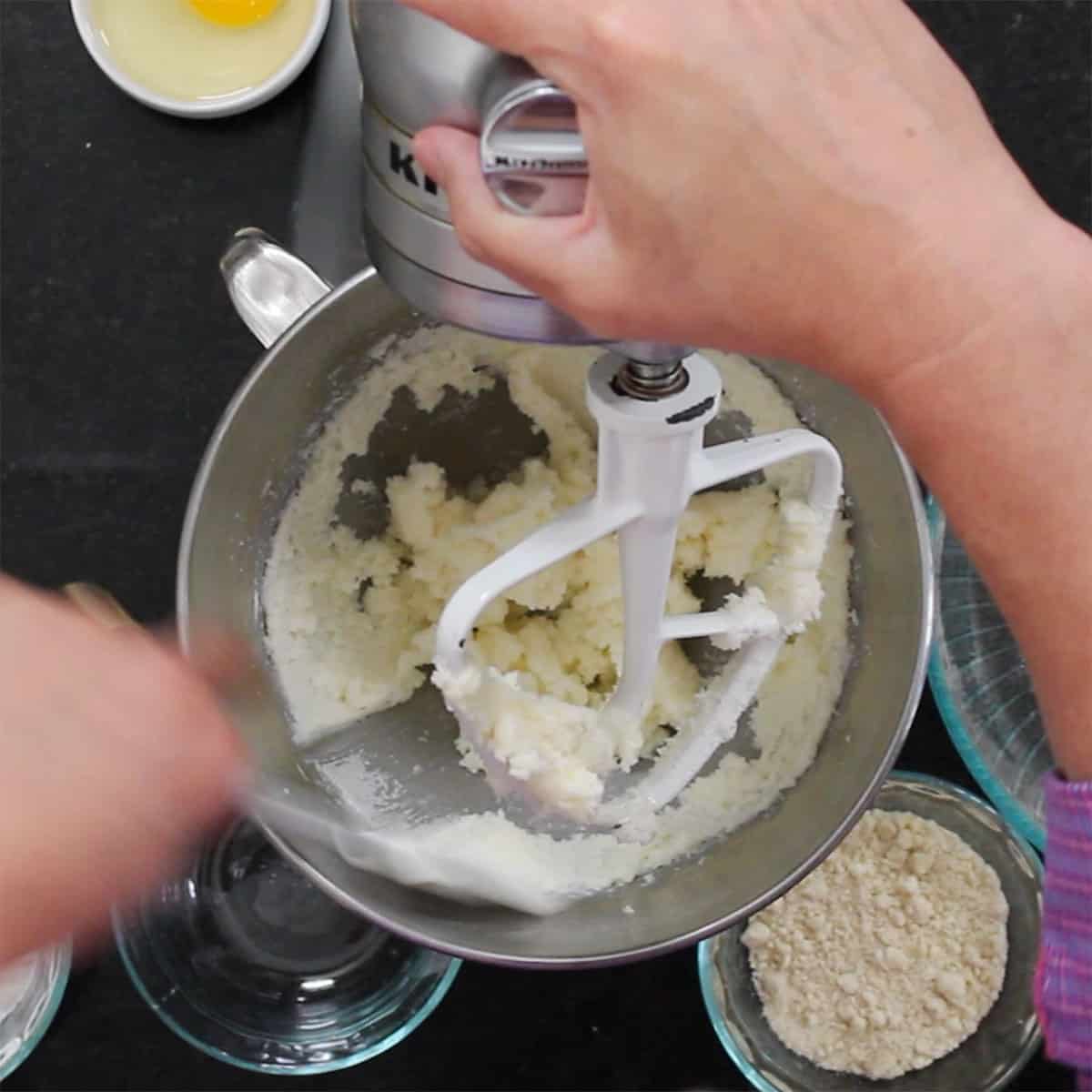 A person beating together softened butter and sugar in the bowl of a stand mixer.