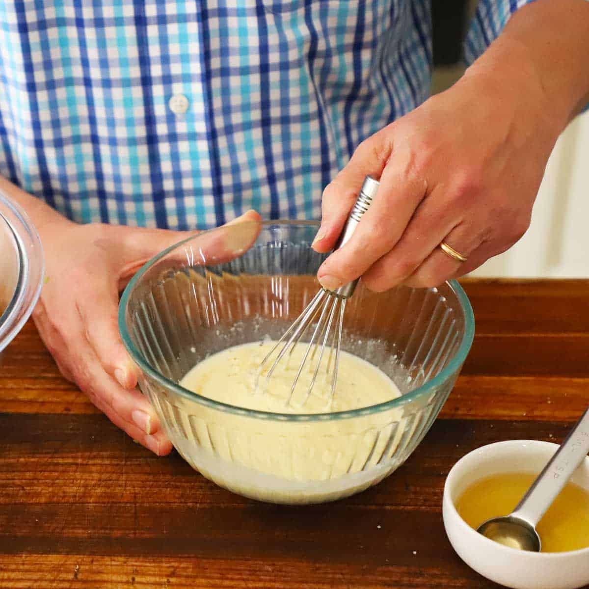 A person using a small whisk to mix together a mayonnaise and Dijon dressing for ham salad.