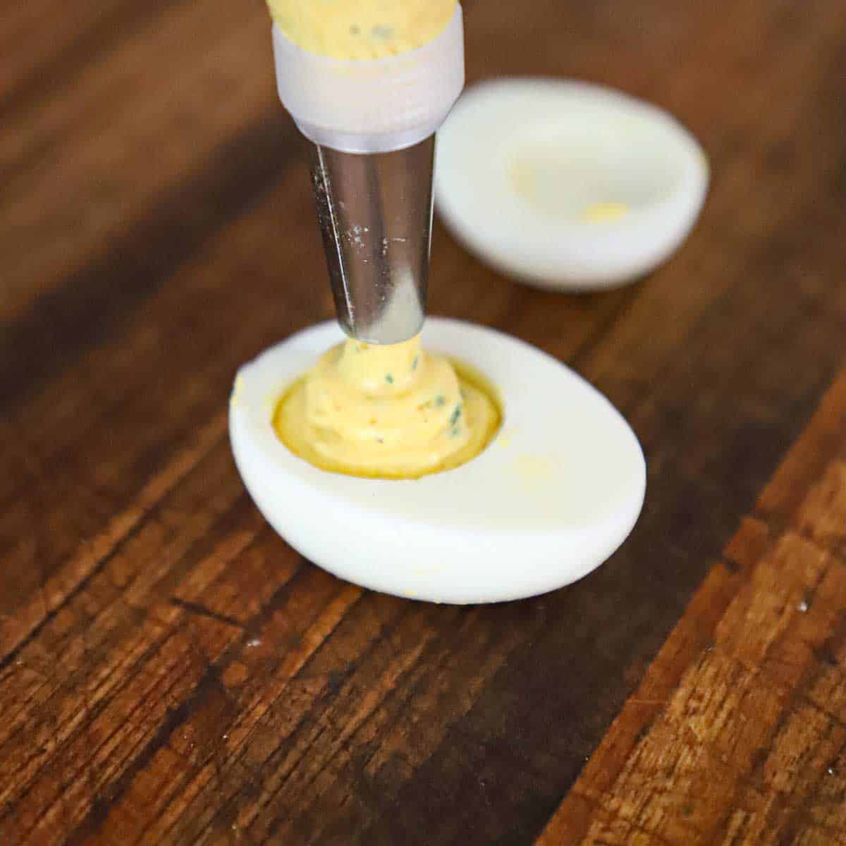 A pastry bag and tip being used to pipe traditional egg filling into a hard boiled egg white.