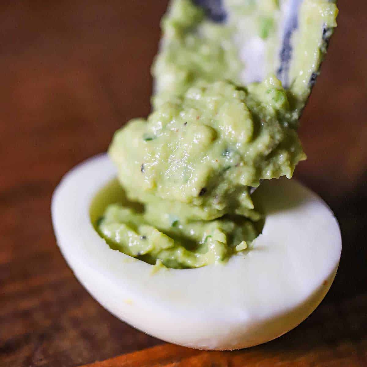 A person transferring an avocado egg mixture into the hollowed out white portion of a hard-boiled egg.