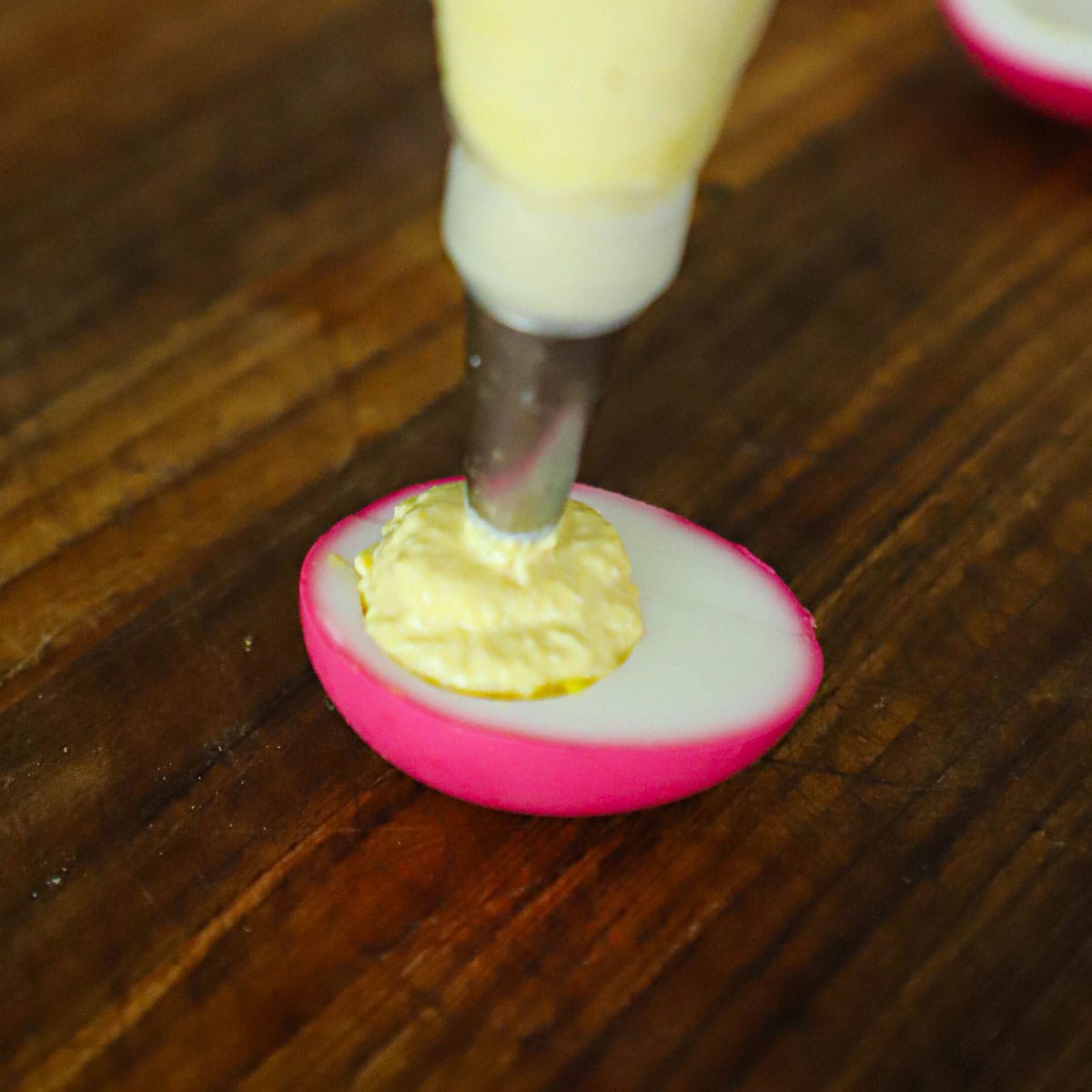 A person piping a horseradish deviled egg filling into a hard boiled egg white that has a red exterior.