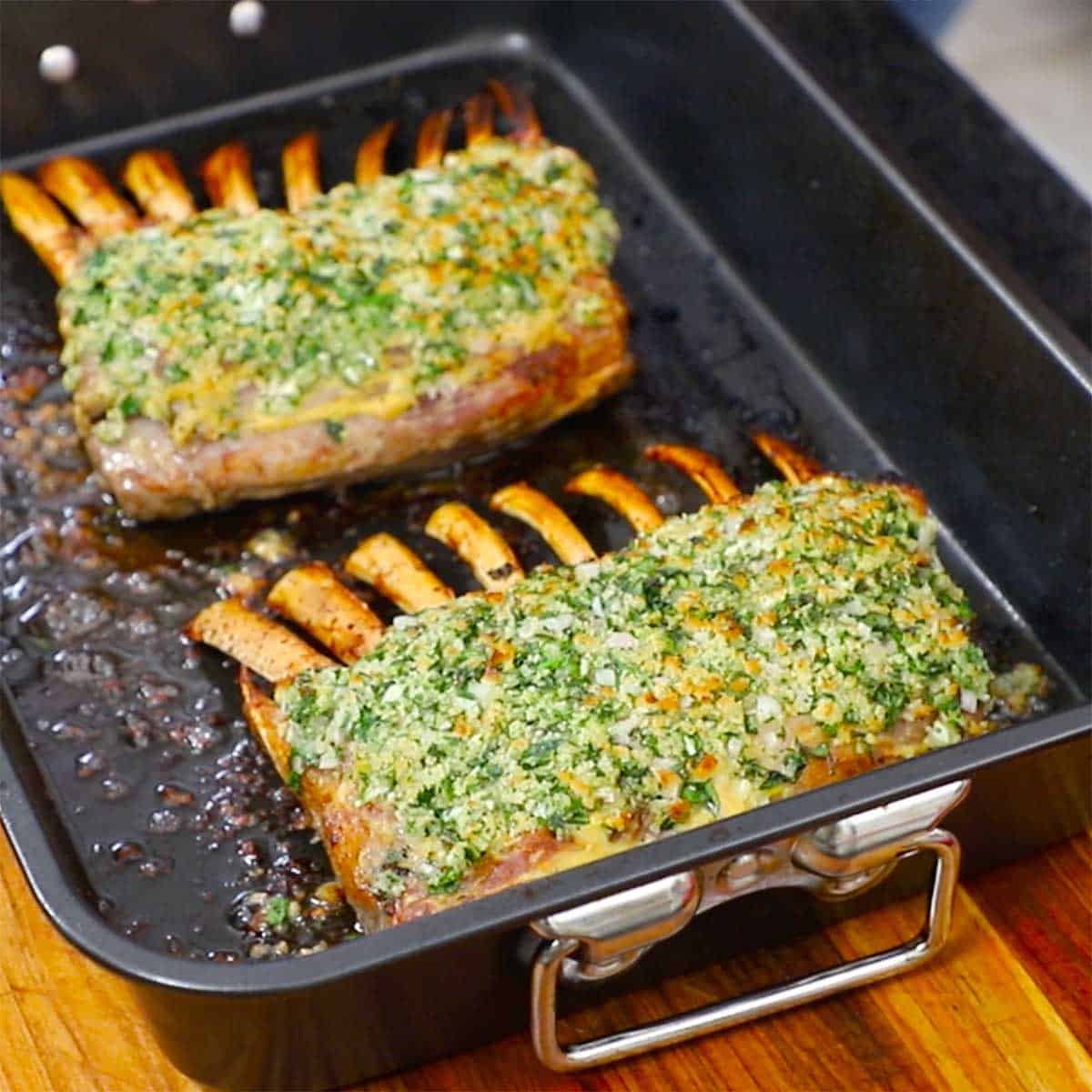 A pair of roast rack of lamb persillade in a black roasting pan.