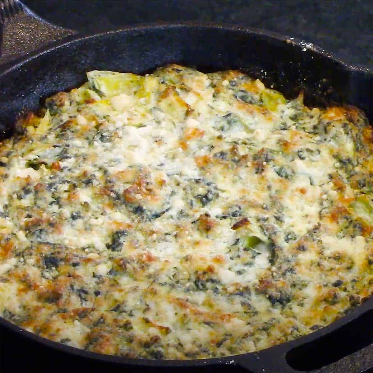 A small cast-iron skillet filled with freshly baked spinach and artichoke dip.