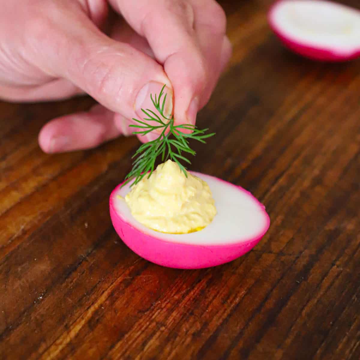 A person placing a fresh dill sprig on top of a horseradish beet deviled egg.