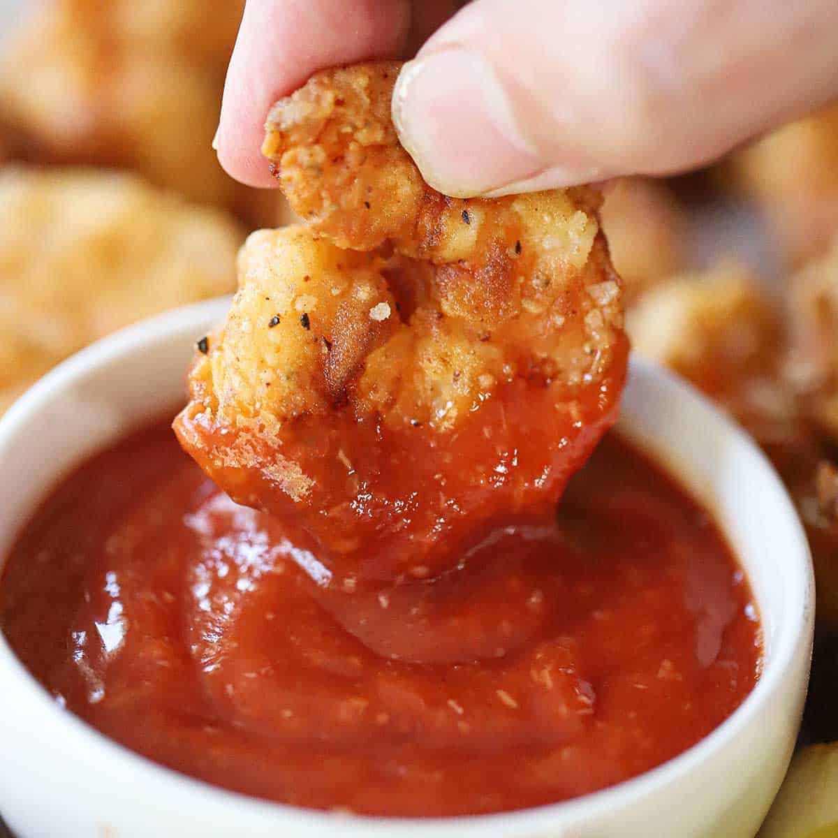 A person plunging a Southern-fried shrimp into a small bowl of homemade cocktail sauce.