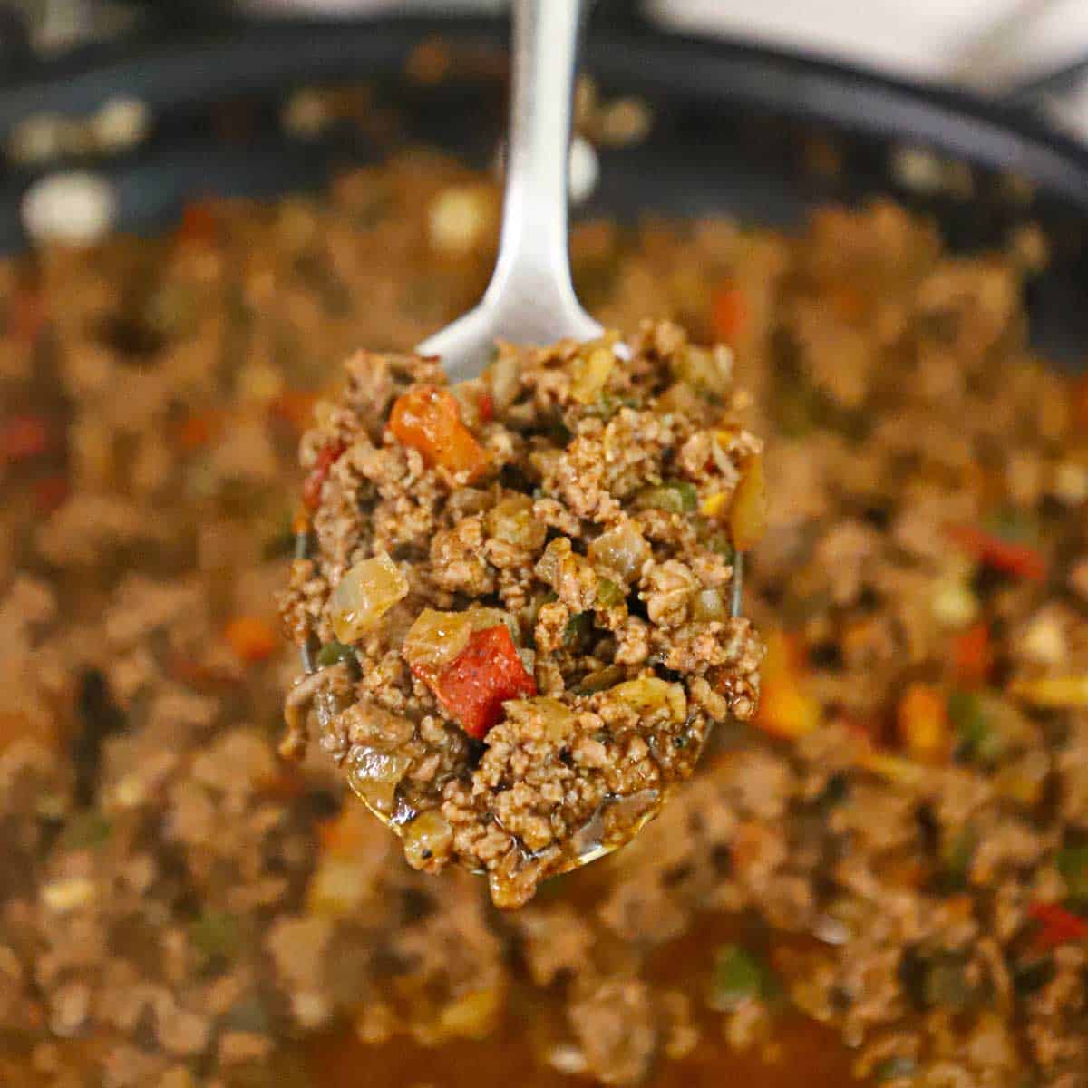 A large spoon holding up a serving of fully cooked beef taco meat.