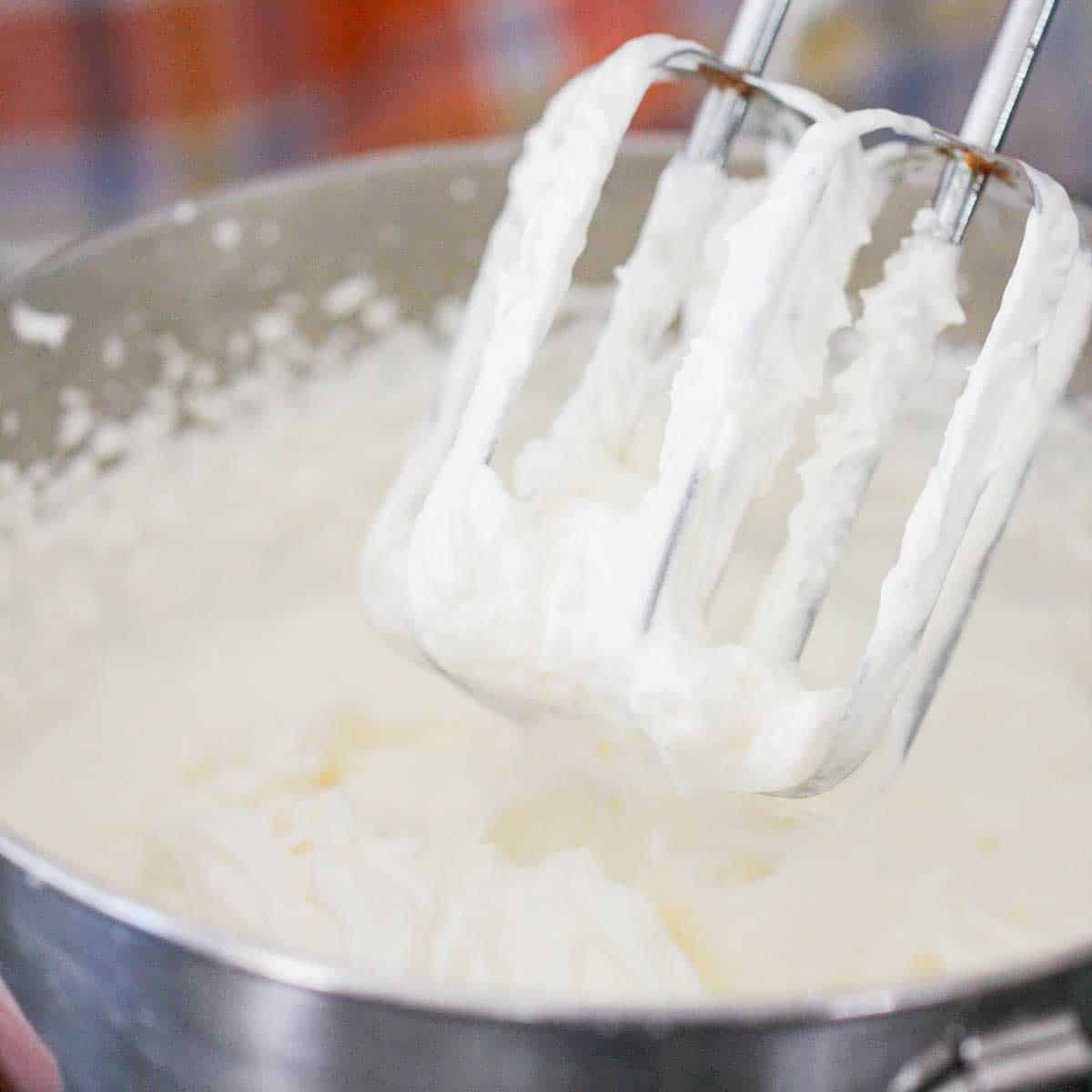 A silver bowl filled with whipped cream with two beaters that have been raised from the whipped cream above it.