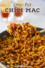 A large serving spoon being used to raise a serving of one-pot chili mac from a skillet of the dish with melty cheese stretching from the spoon into the skillet.