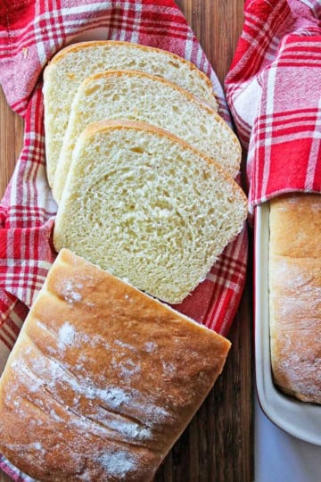 A red and white plaid napkin with several slices of county white bread on it next to the remaining unsliced loaf.