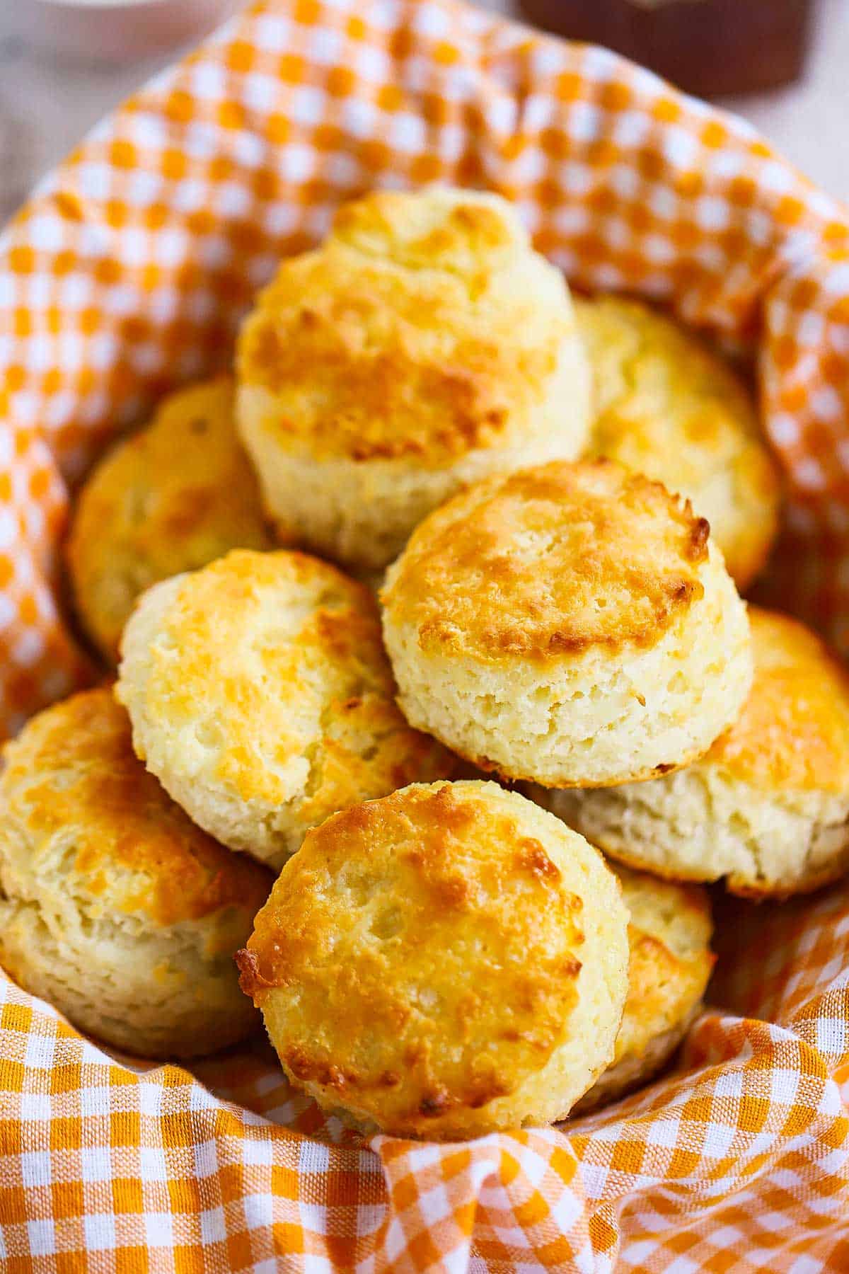 A pile of Southern buttermilk biscuits in a basket lined with a orange and white checkered cloth napkin.