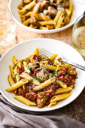 Two white pasta bowls sitting next to each other both filled with a serving of pasta with roasted tomatoes and pesto chicken.