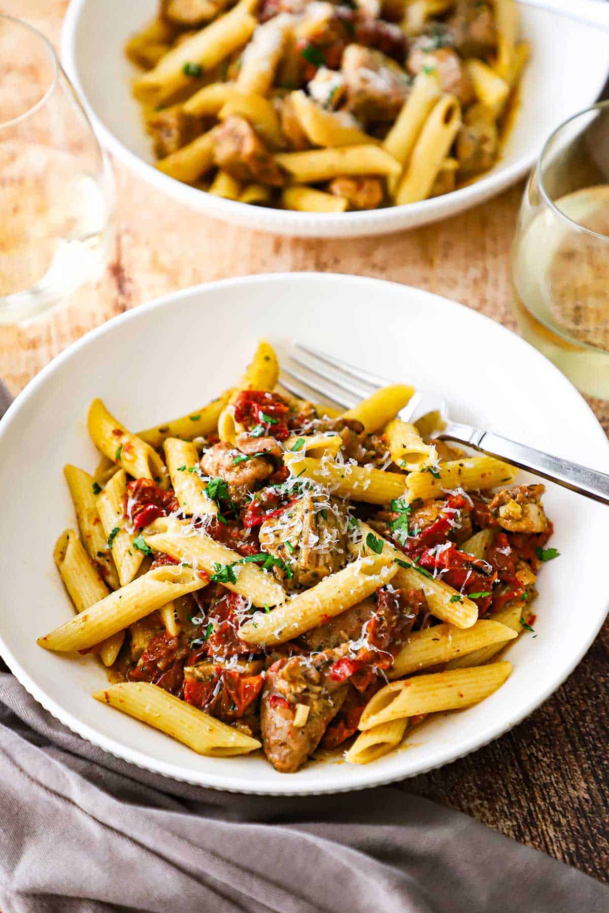 Two white pasta bowls sitting next to each other both filled with a serving of pasta with roasted tomatoes and pesto chicken.