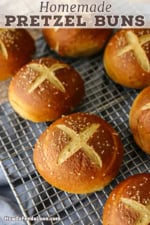 Two rows of freshly baked homemade pretzel buns cooling on wire baking rack on a grey linen.