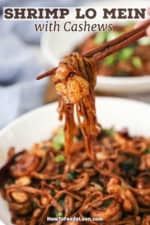 A person using a pair of chopsticks to hold up a bite of shrimp lo mein with cashews.