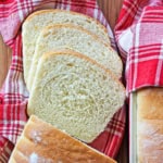 A red and white plaid napkin with several slices of county white bread on it next to the remaining unsliced loaf.