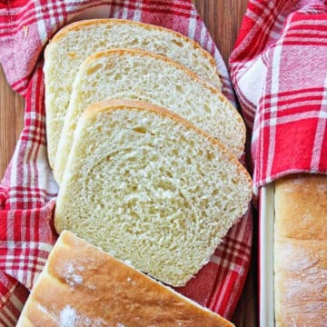 A red and white plaid napkin with several slices of county white bread on it next to the remaining unsliced loaf.