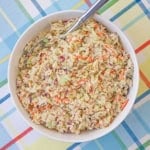 An overhead view of a bowl of diner-style coleslaw with a serving spoon inserted into the side of the dish.