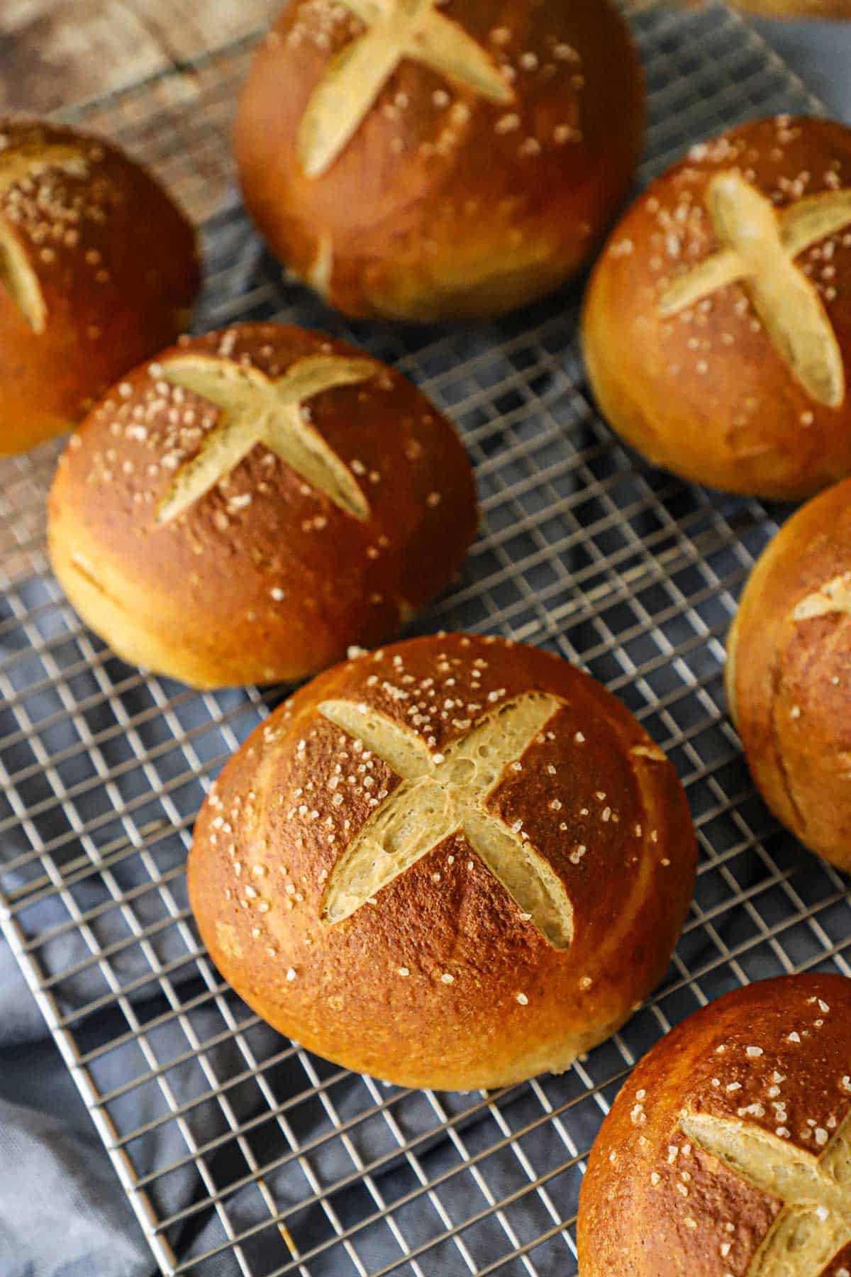 Two rows of freshly baked homemade pretzel buns cooling on wire baking rack on a grey linen.