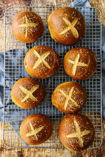 An overhead view of six homemade pretzel buns resting on a wire baking rack.
