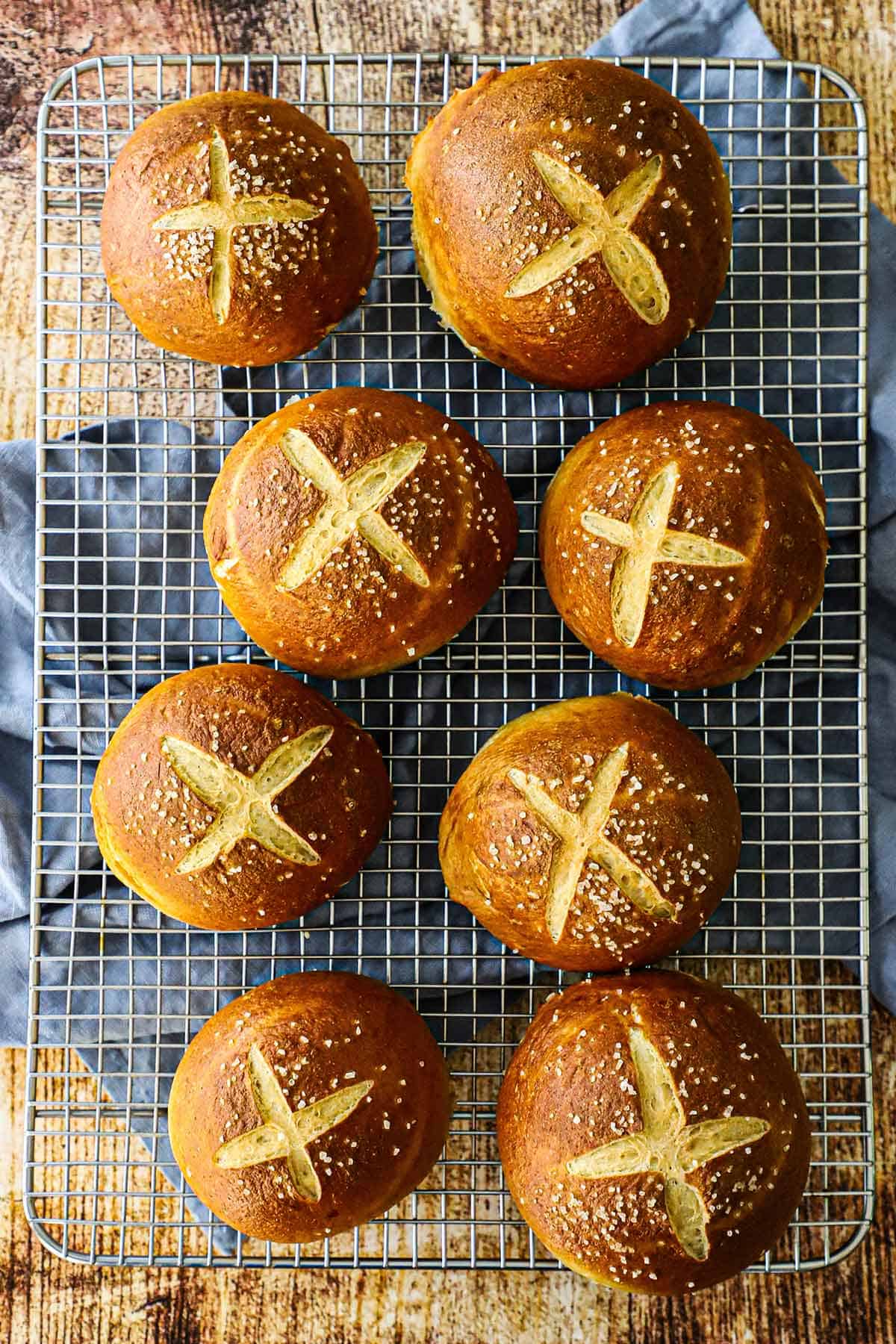 An overhead view of six homemade pretzel buns resting on a wire baking rack.