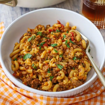A white bowl filled with a serving of one-pot chili mac with a gold fork inserted into the side of the food.