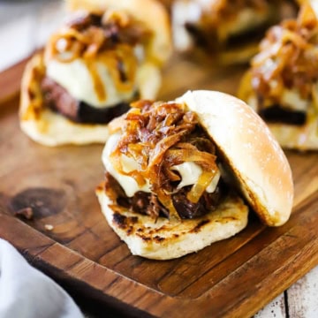 A pot roast slider topped with melty Swiss cheese, caramelized onions, and a toasted slider bun resting on the side of the pot roast.
