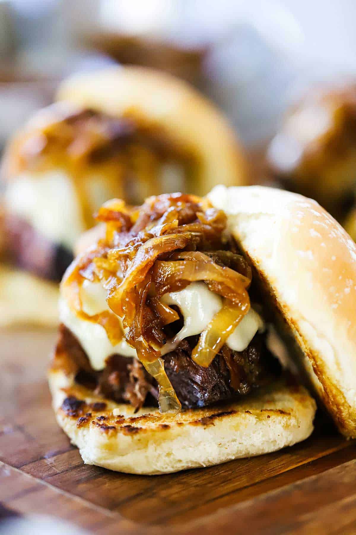 A pot roast slider topped with melty Swiss cheese, caramelized onions, and a toasted slider bun resting on the side of the pot roast.