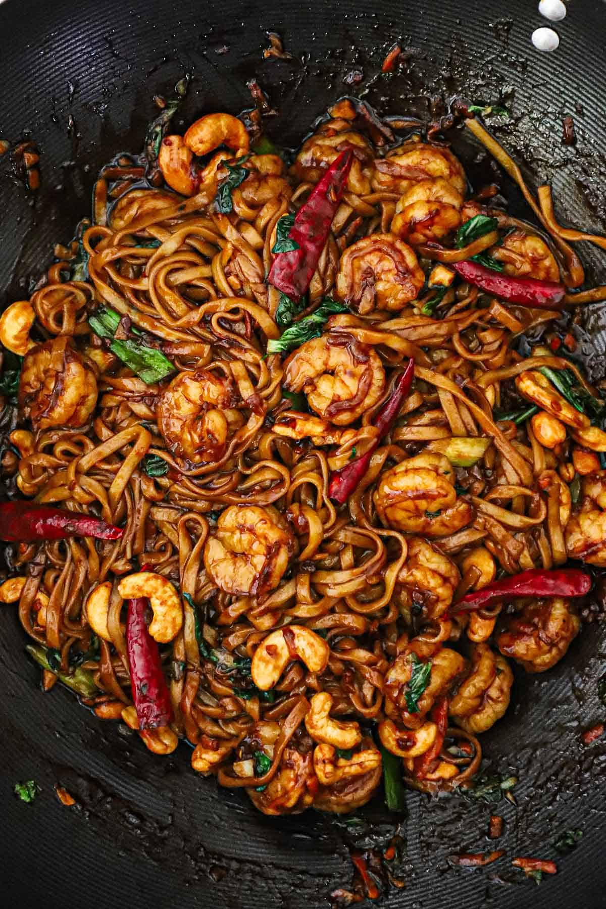 A black wok filled with shrimp lo mein with cashews and Chinese red peppers.