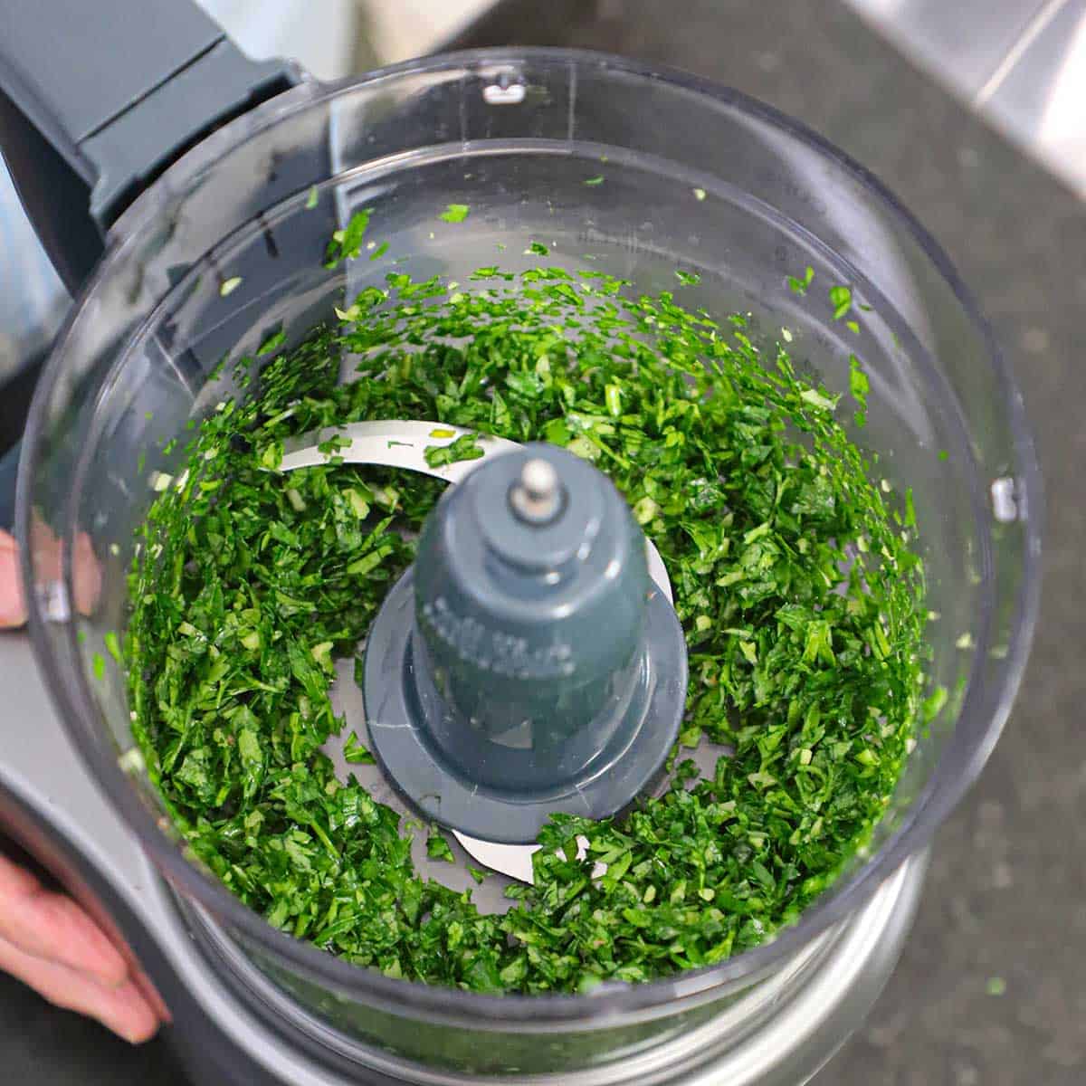 The inside of a food processor that is filled with parsley and garlic that has been finely chopped with food processor.