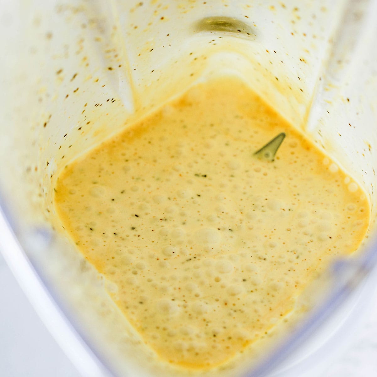Hollandaise sauce in the bottom of a blender with the point of one the blades slightly visible.