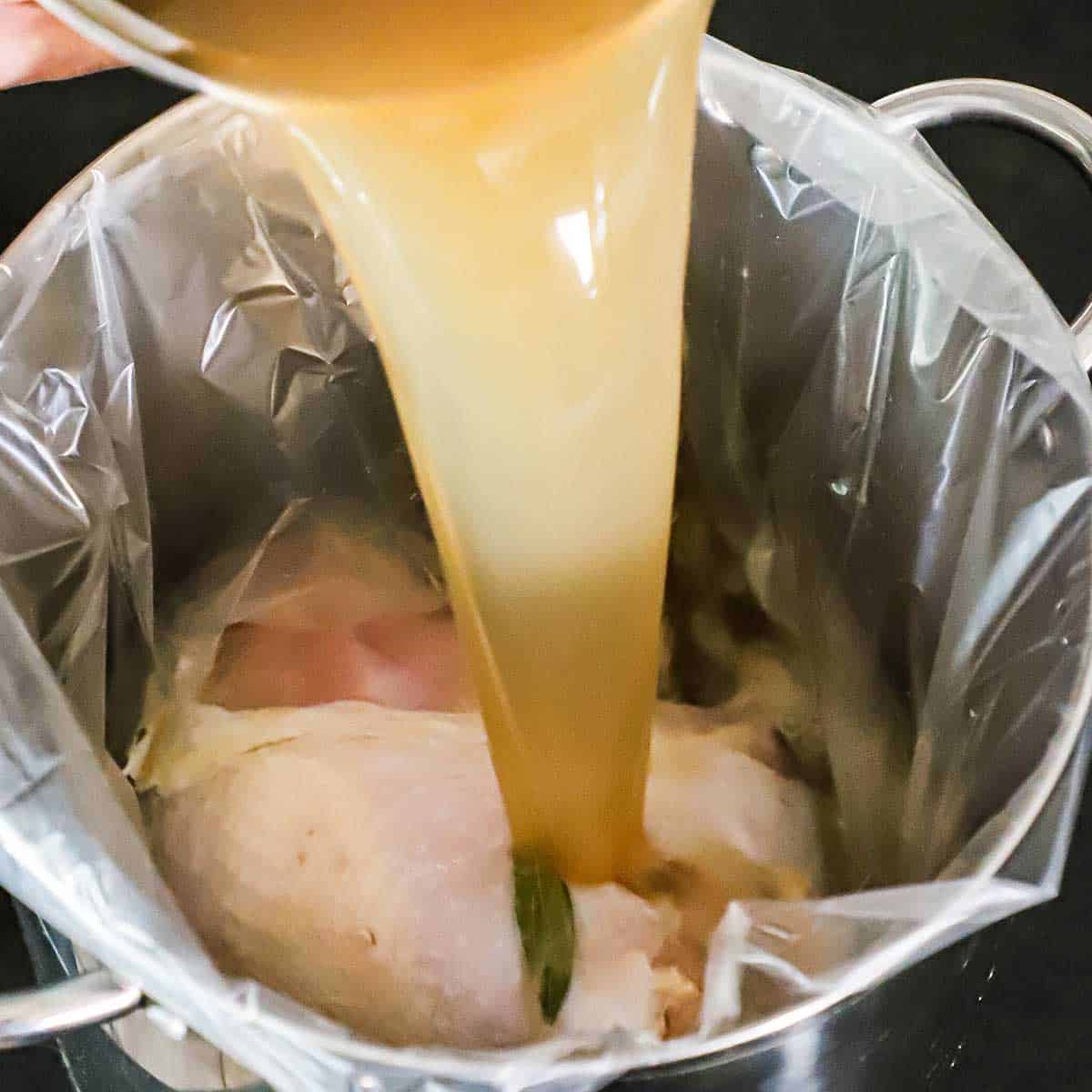 A person pouring a turkey brine over a whole turkey breast that is in the bottom of a brine bag in a large stock pot.