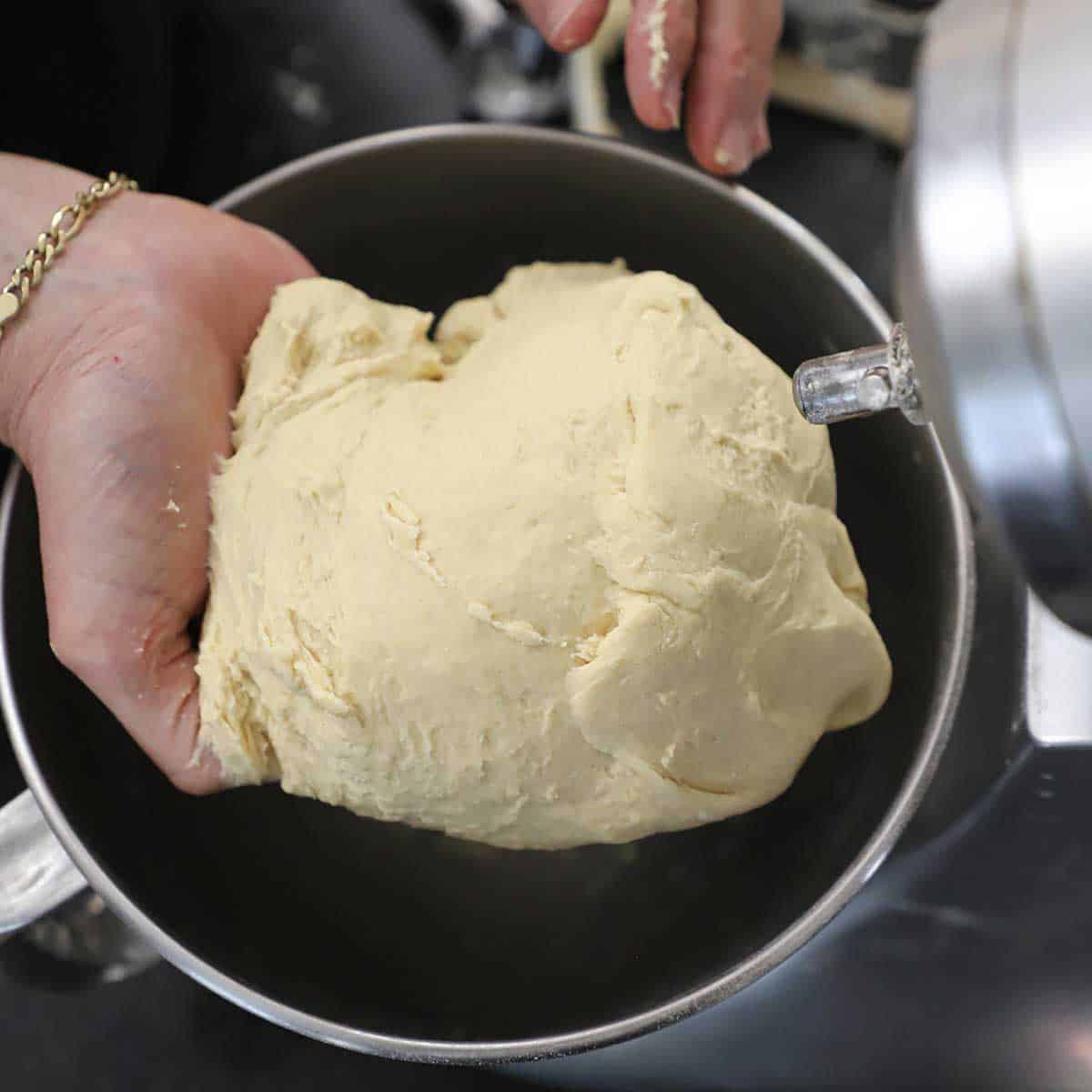 A person pulling a ball of pretzel dough from the bowl of a stand mixer.