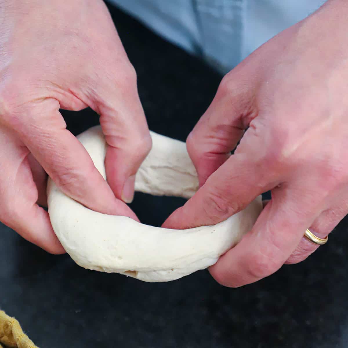 A person using his thumb and fingers to stretch bagel dough into a circular bagel formation.