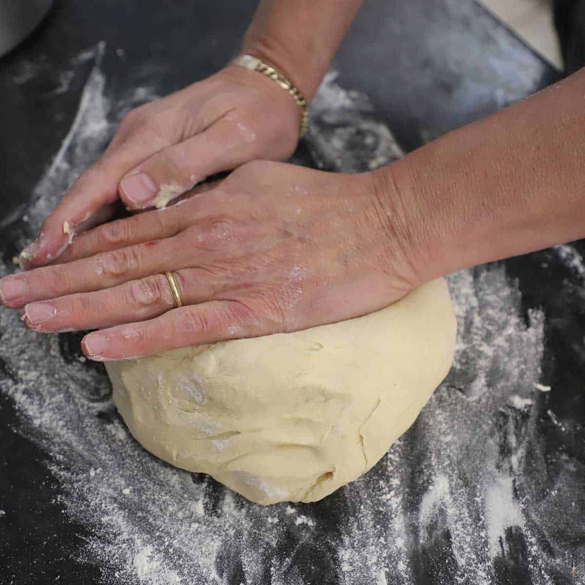 A person using the palms of his hands to knead pretzel dough on a floured black marble countertop.