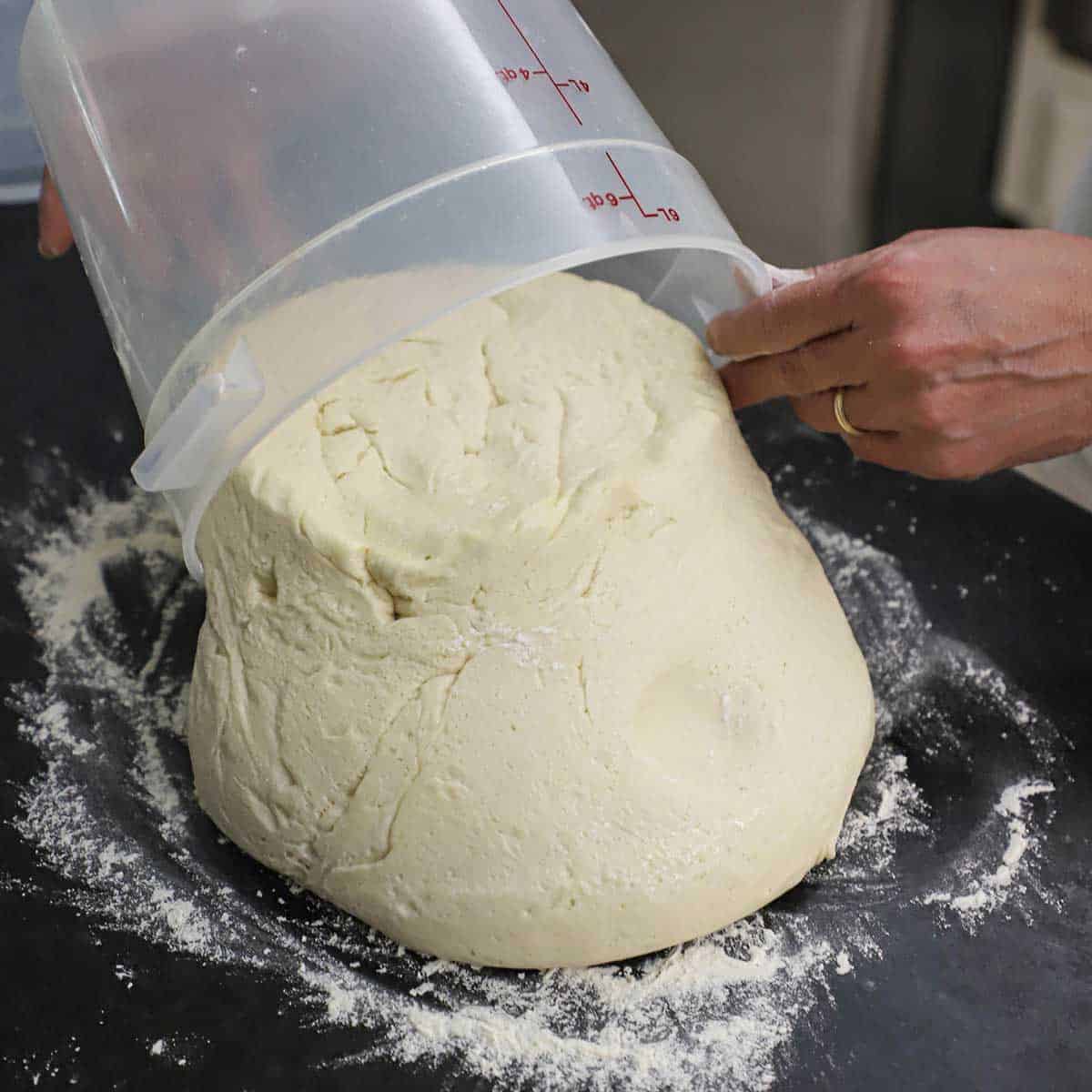 A person transferring risen bread dough onto a black marble countertop that has been lightly floured.