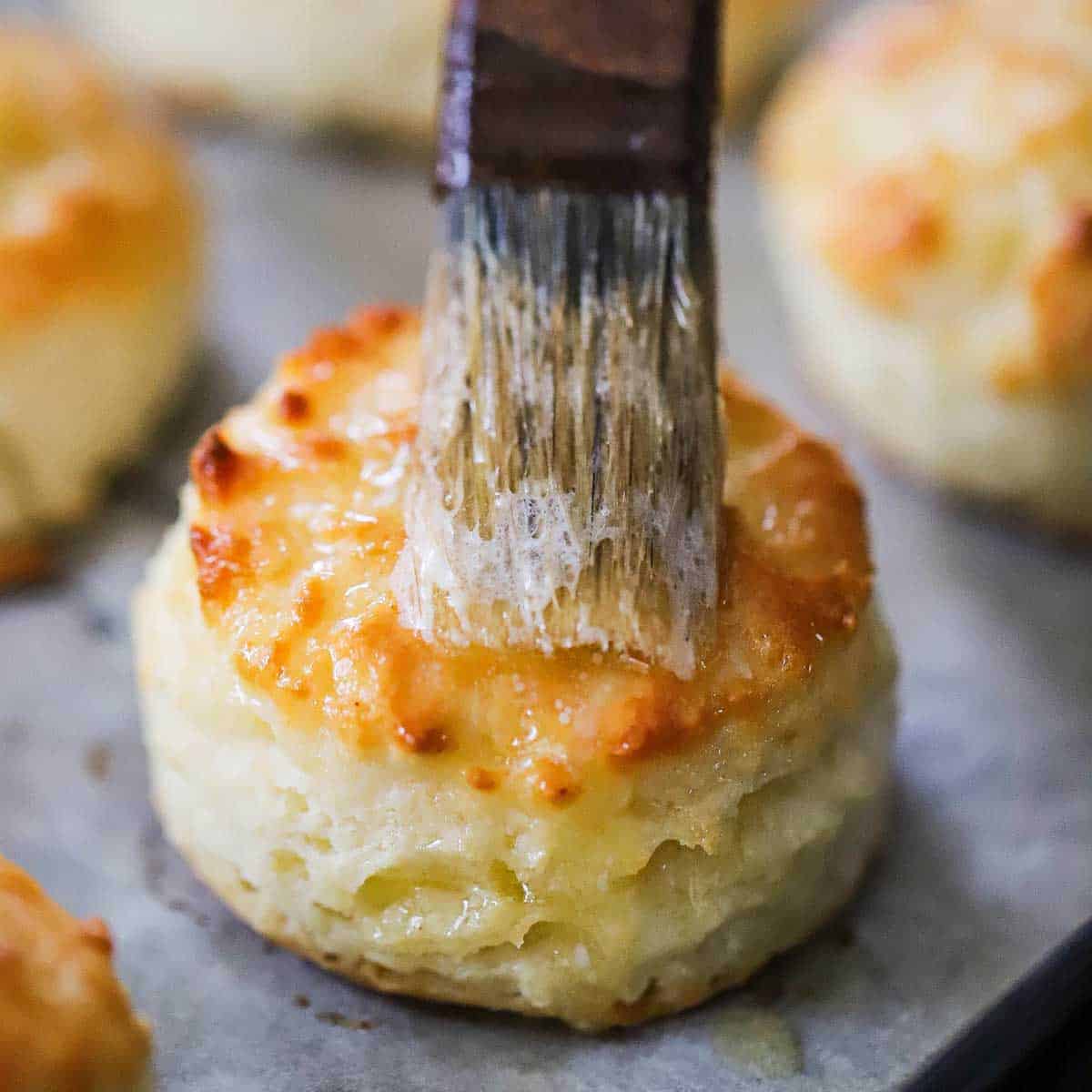 A pastry brush being used to apply melted butter over the top of a freshly baked Southern buttermilk biscuit.