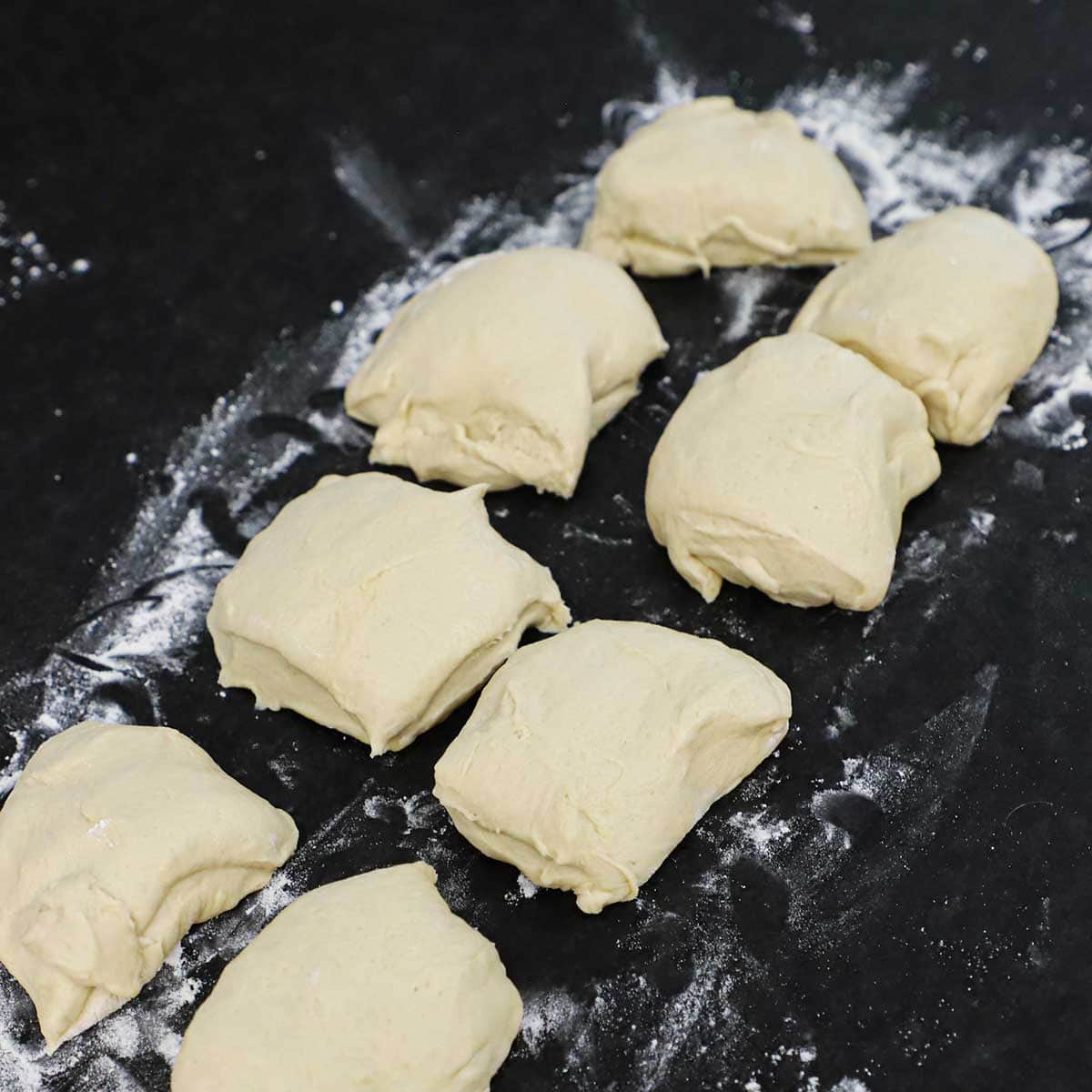 Eight square of pretzel dough on a lightly floured black marble countertop.