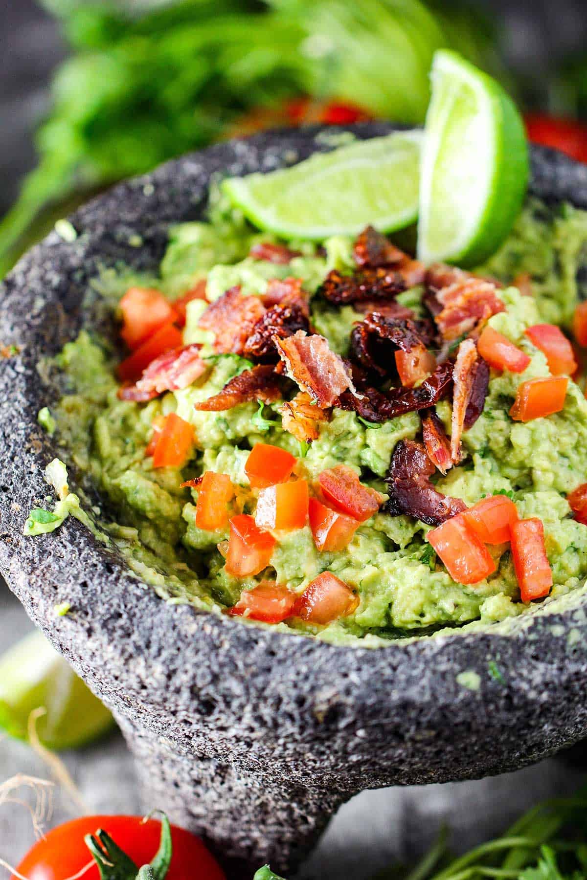 Best-ever guacamole in a black molcajete and topped with chopped tomatoes, bacon, and lime wedges.