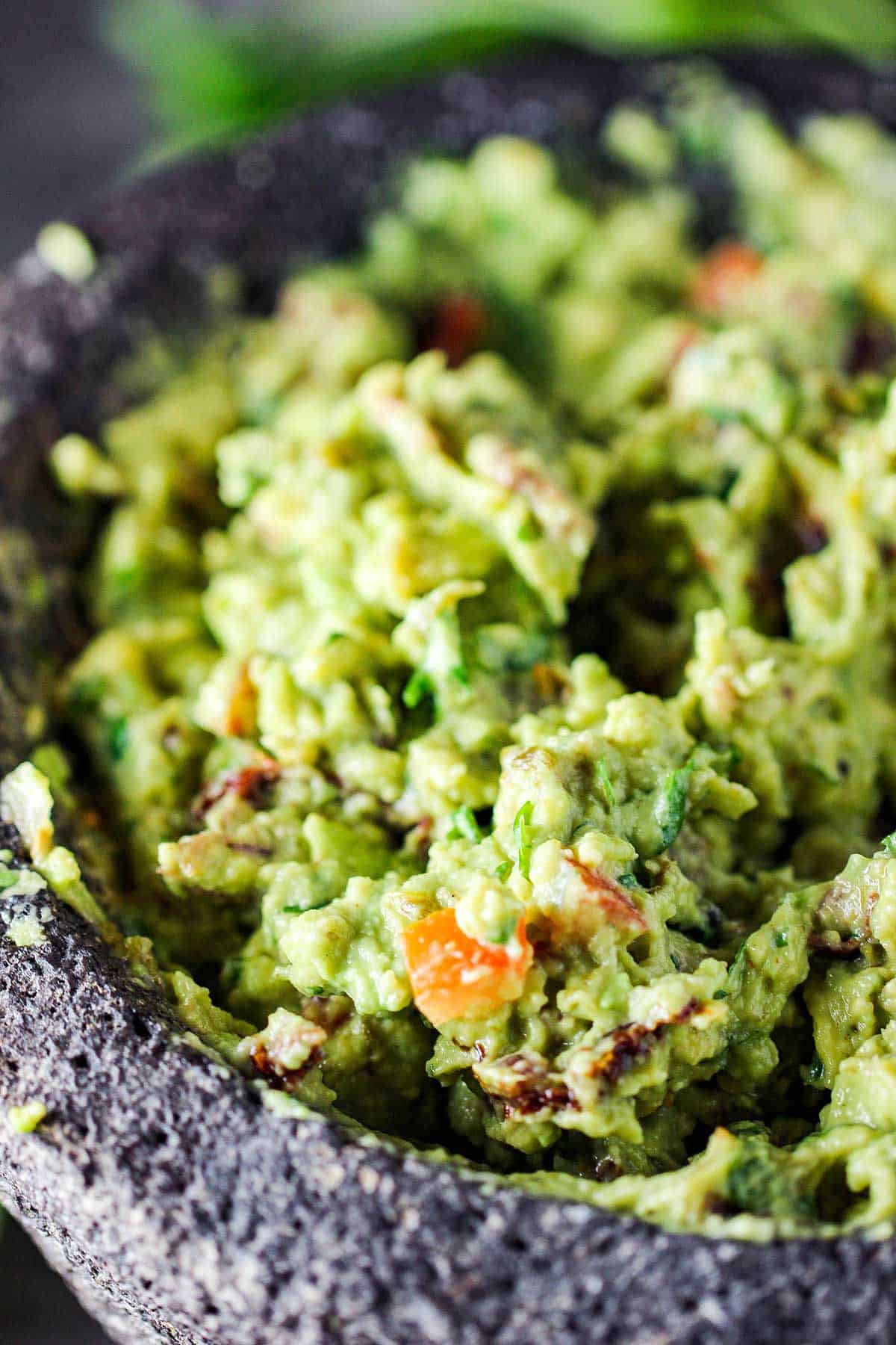 Freshly made guacamole with avocados, tomatoes, cilantro, and peppers in a molcajete.