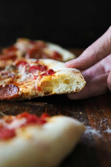 A person holding up a slice of New York-style pizza revealing the nooks and crannies in the edge of the crust.