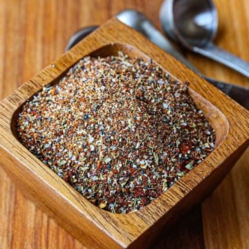 A small square wooden bowl filled with homemade taco seasoning sitting on a wooden cutting board.
